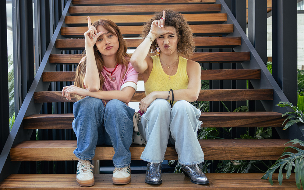 Azul Guaita y Pamela Moreno sentadas en unas escaleras haciendo un gesto divertido en la serie El otro padre.